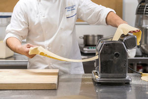 Morris Inn Banquet - A chef is making homemade pasta through a pasta machine.