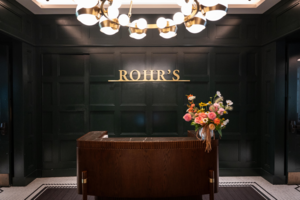 Rohr's entrance - a large gold Rohr's sign hangs over the wooden check-in table. A bouquet of pink, orange, yellow, and white flowers sit on the counter.