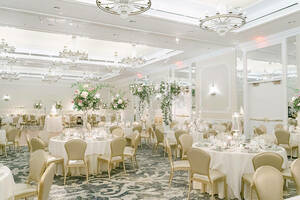 Smith Ballroom Wedding - circular tables with white tablecloths, glassware, and white and green flowers fill the room. Crystal chandeliers hang from the ceiling.